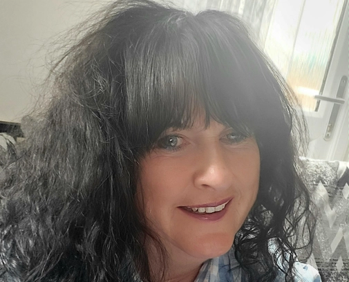 woman with dark curly hair and fringe smiling into the camera